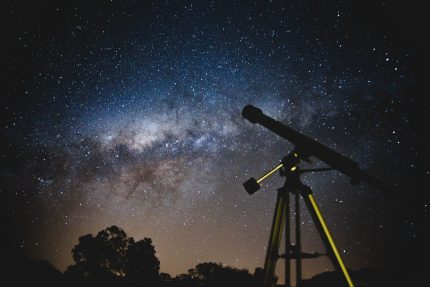 Telescope silhouetted against a starry night sky